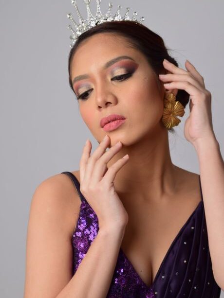 Ladyboy in a purple sequin dress and tiara, touching her face gently