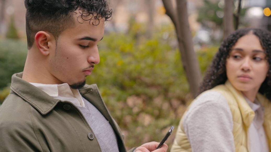 Man looking at his phone while a woman beside him looks away.