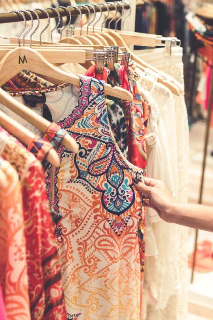 Hand selecting a colorful patterned dress from a clothing rack.