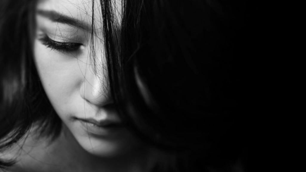 Close-up of a woman's face, looking down with hair partially covering her face.