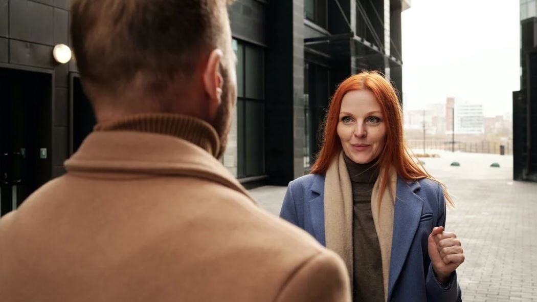 Red-haired woman smiling while talking to a man outside an office building.