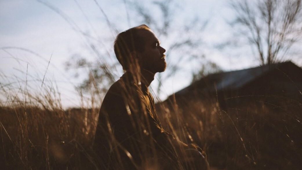 Person sitting quietly in a field during sunset, with a serene expression.