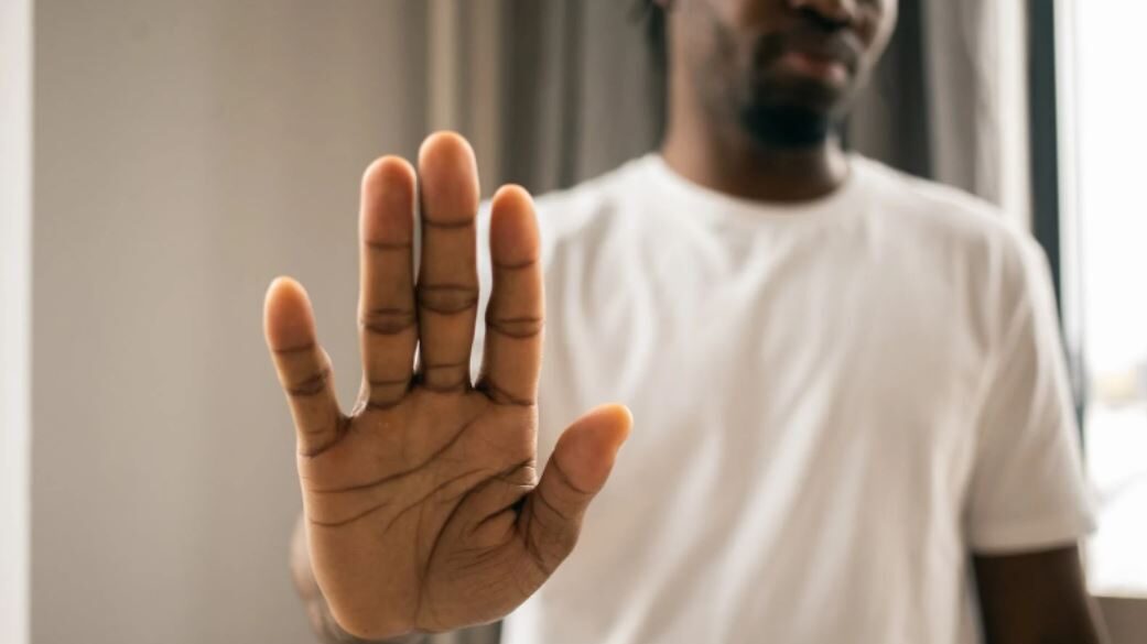 Person holding up a hand in a stop gesture, with a blurred face in the background.