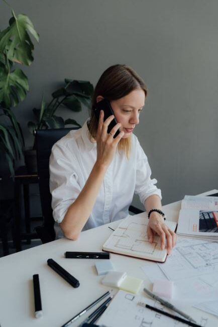 Woman on the phone working at a desk with papers and a notebook.