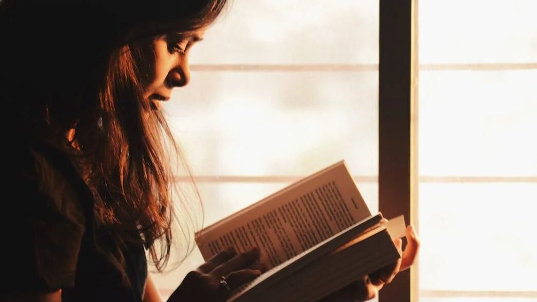 Close-up of a woman reading a book, illuminated by warm natural light.