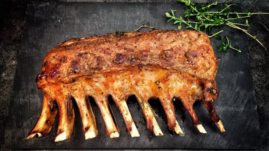 Rack of roasted ribs garnished with fresh herbs on a dark background.