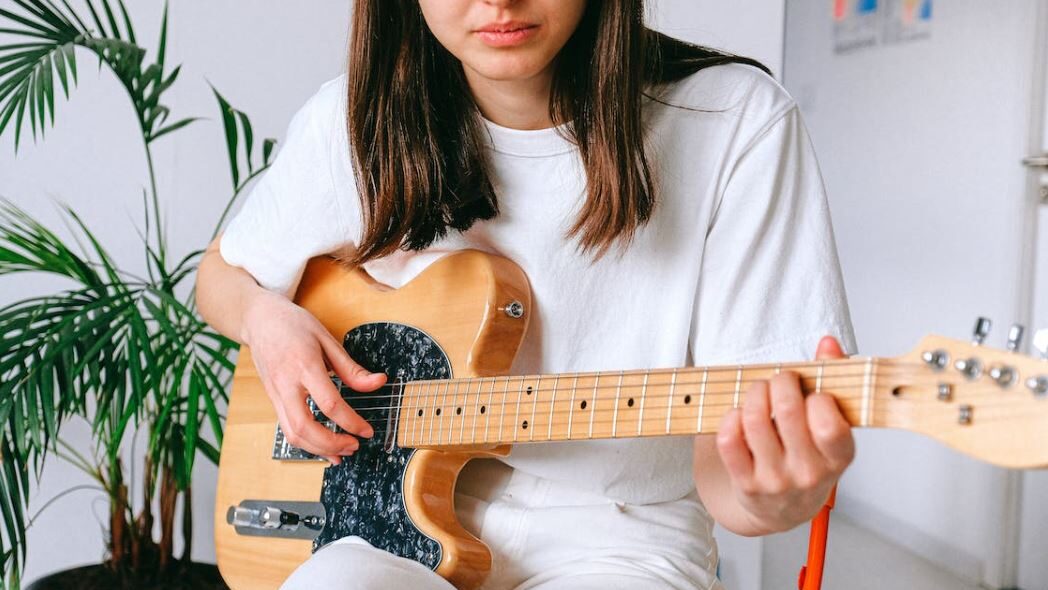 Close-up of a woman strumming an electric guitar in a relaxed setting.