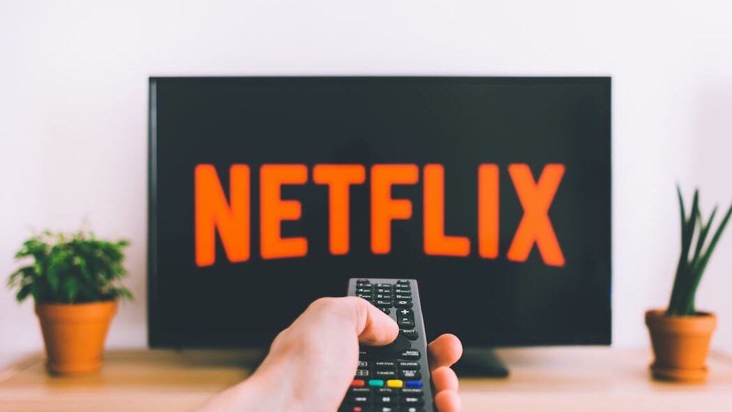 Remote control aimed at a television displaying the Netflix logo on the screen.