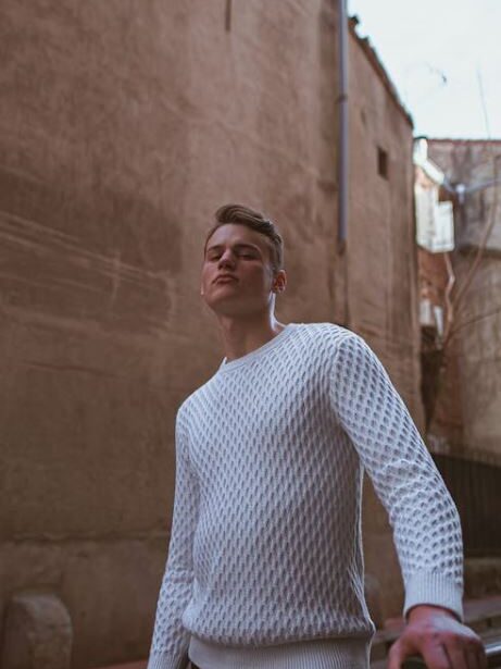 Man wearing a textured sweater, looking confident while walking through a narrow alley.