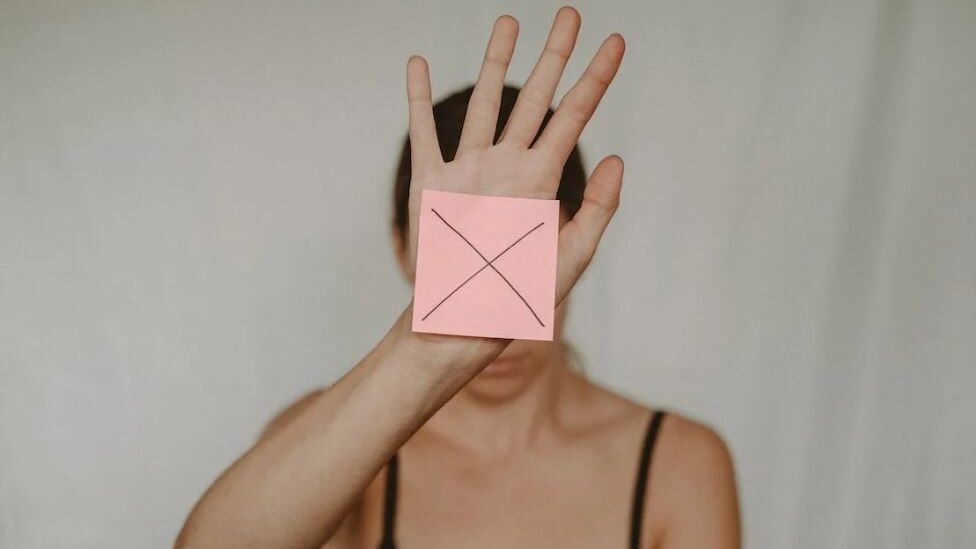 The image shows a person holding up an "X" on a sticky note, symbolizing a clear refusal or boundary being set.