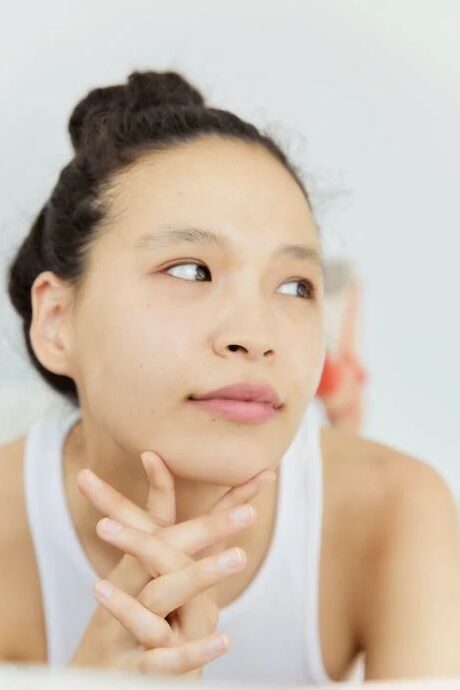 A close-up of a woman resting her chin on her clasped hands, gazing thoughtfully into the distance.