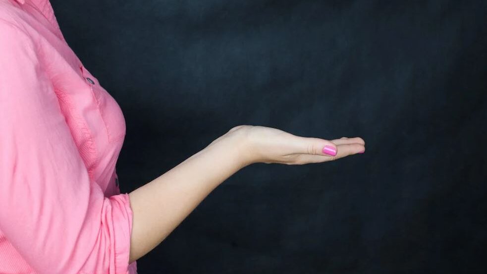 Side view of a woman’s open hand, palm facing up, dressed in pink, suggesting gesture or invitation.