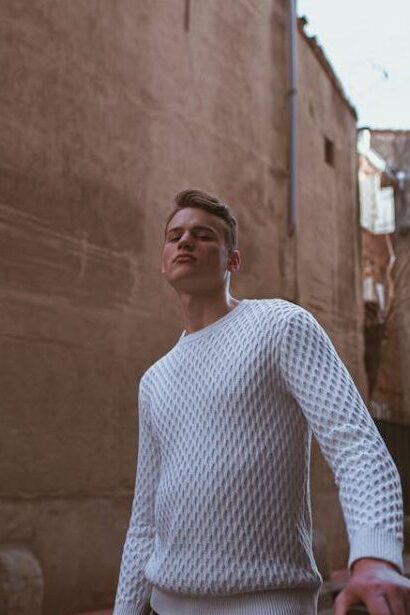 Man in a white sweater standing in an alley, looking directly at the camera.