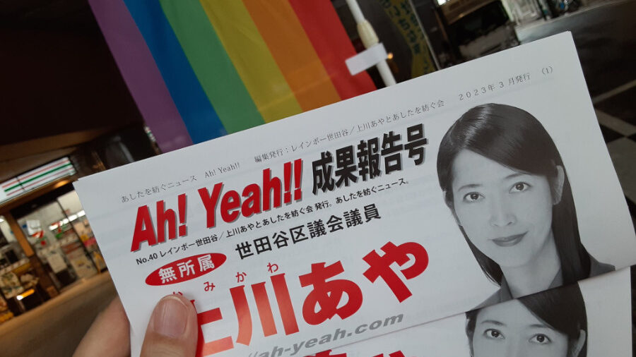 Close-up of campaign materials for Kamikawa Aya, featuring her portrait and the phrase 'Ah! Yeah!!' against a rainbow flag background. Taken in preparation for her public speeches resuming in Tokyo.