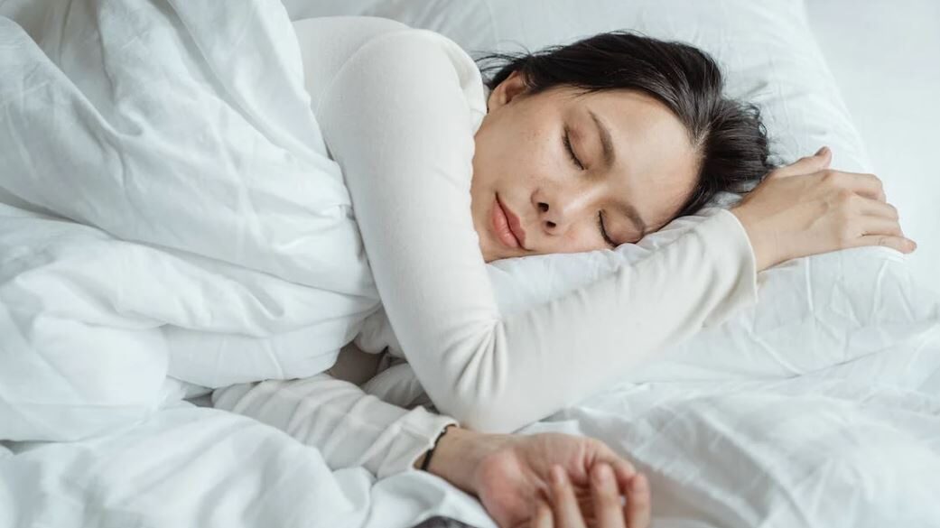 A serene moment captured of a woman asleep on her side, surrounded by white sheets.