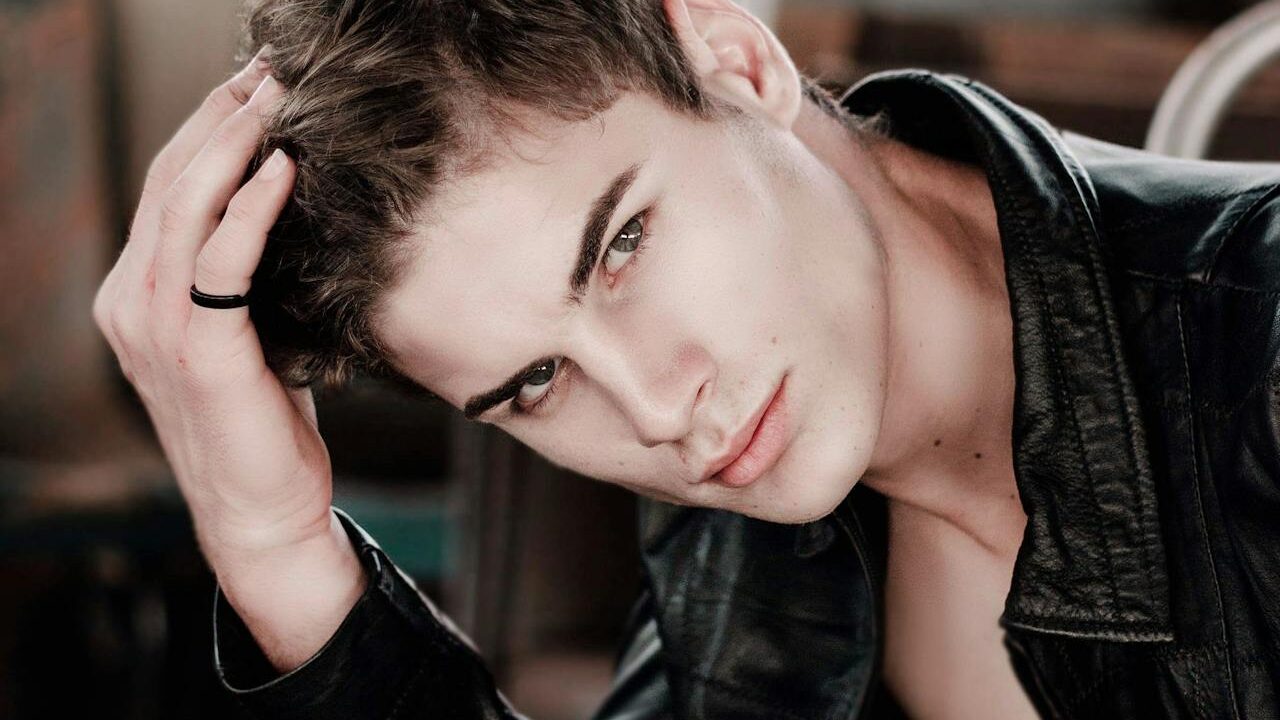 A stylish young man with a black ring and dark leather jacket, captured in a thoughtful yet bold expression with soft indoor lighting.