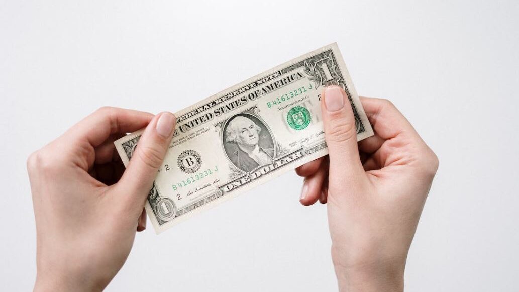 Two hands holding a one-dollar bill against a plain white background.