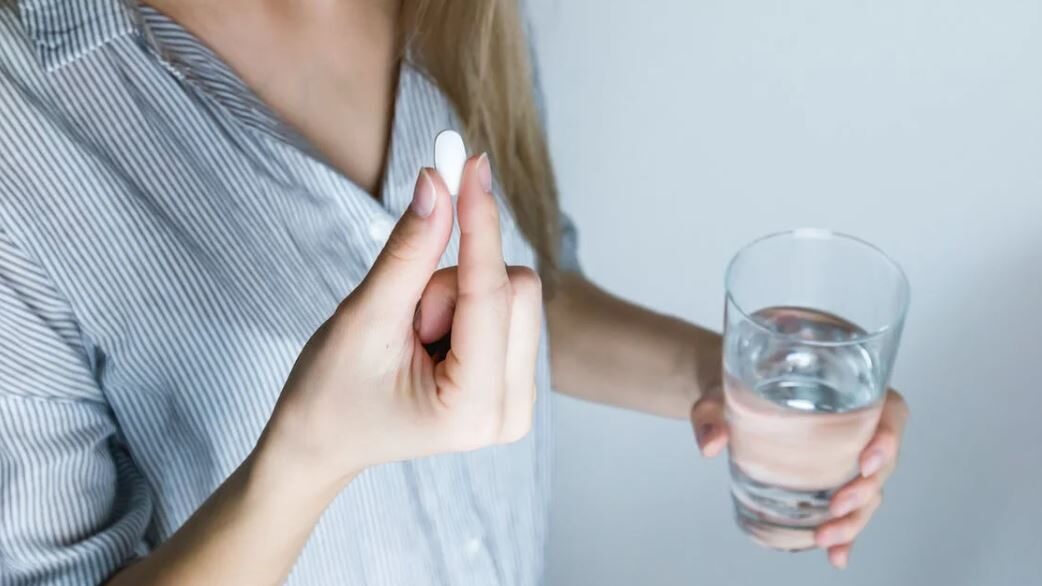 A person holding a pill in one hand and a glass of water in the other, ready to take medication.