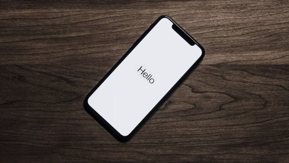 A modern smartphone welcoming the user with "Hello," set on a smooth wooden backdrop.