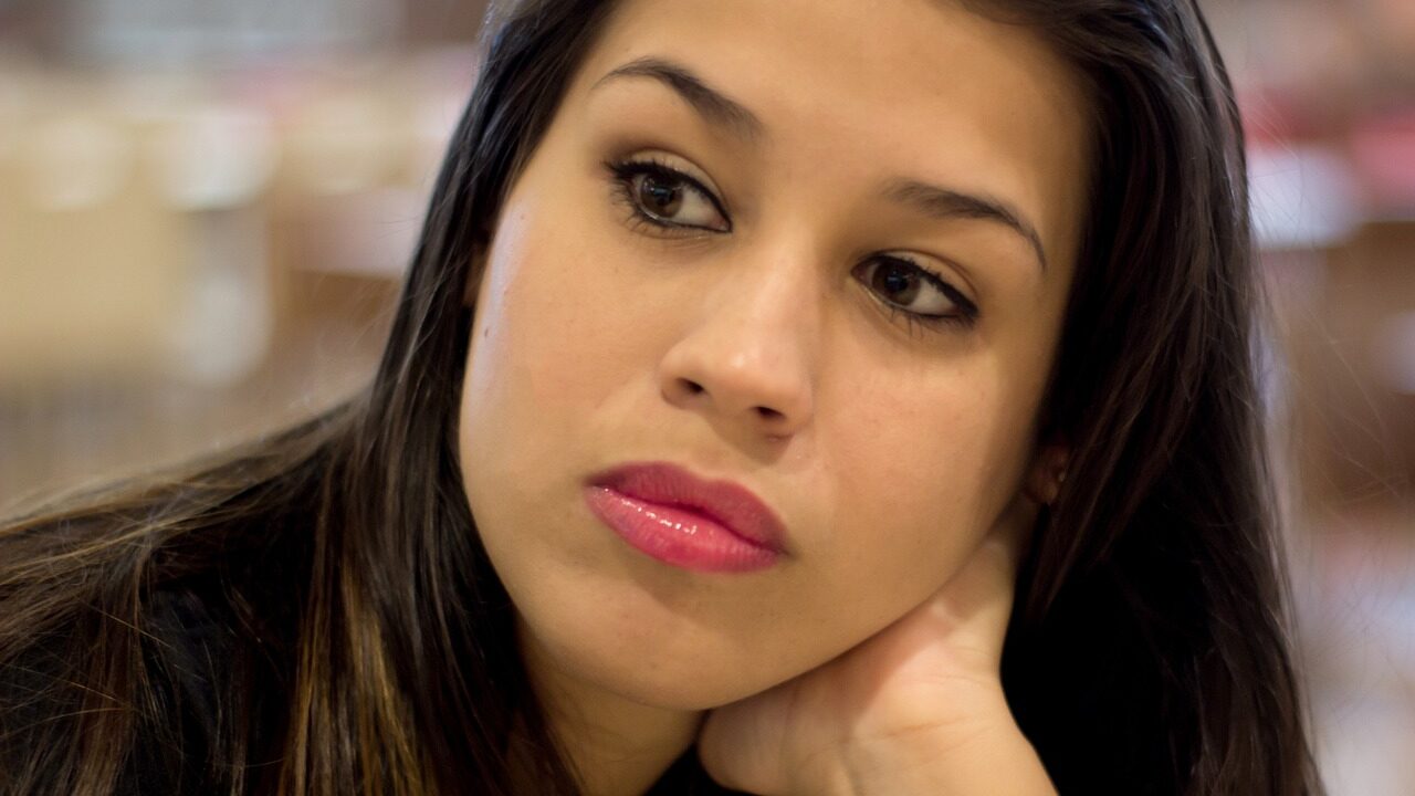 Woman with long dark hair resting her chin on her hand, looking thoughtfully into the distance.