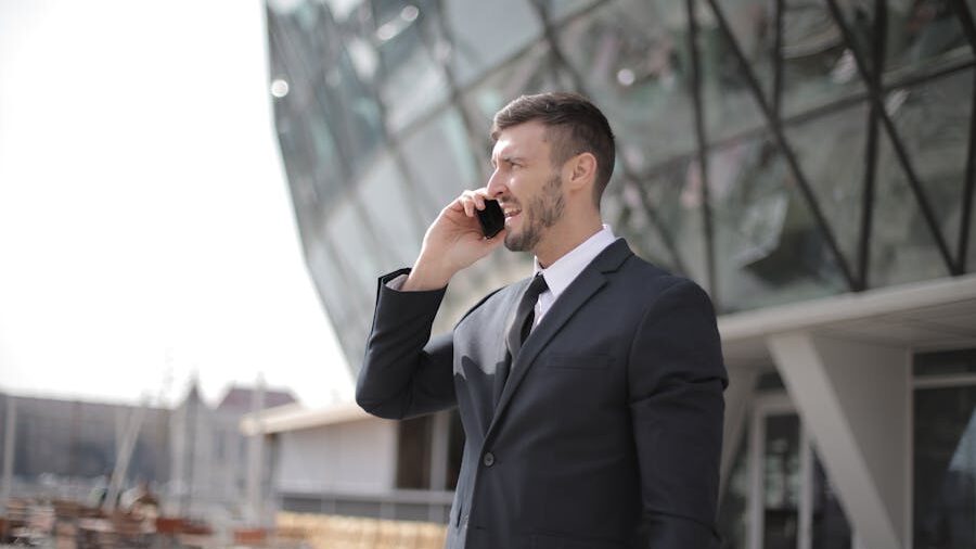 A professional in formal attire standing outside and engaged in a conversation on his phone.