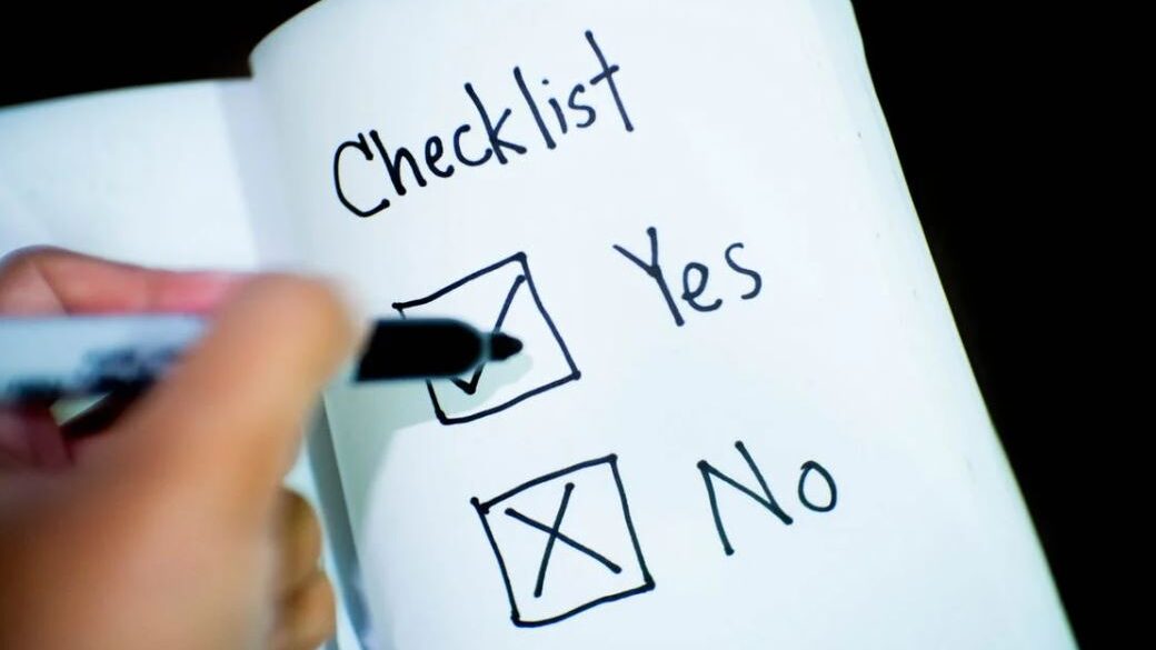 A handwritten checklist in a notebook, with "Yes" checked and "No" crossed out, and a hand holding a marker.