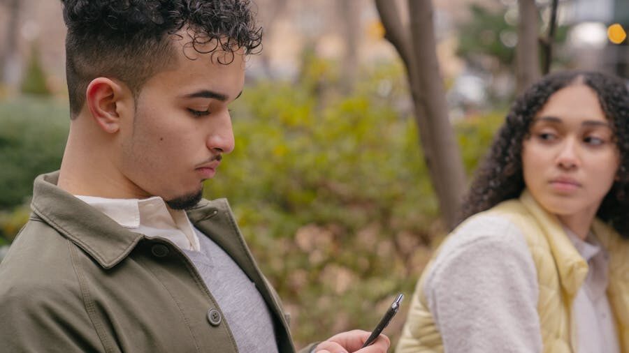 Outdoor scene with a young man checking his phone and a woman glancing in his direction.