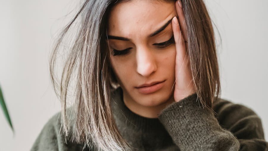 Woman with shoulder-length hair wearing a dark sweater, touching her temple with a concerned expression.