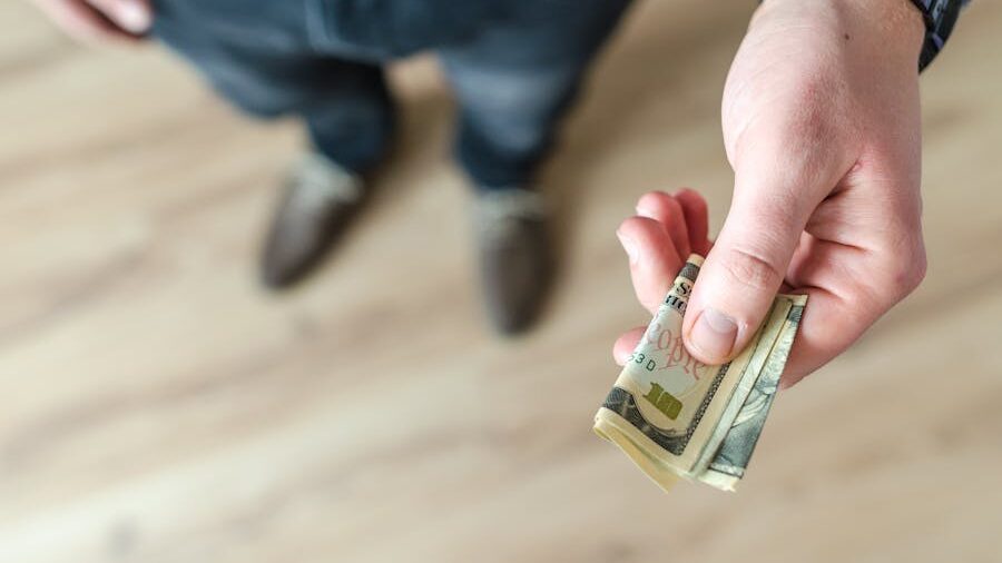 Person extending a folded stack of US dollars, seen from a high-angle perspective.