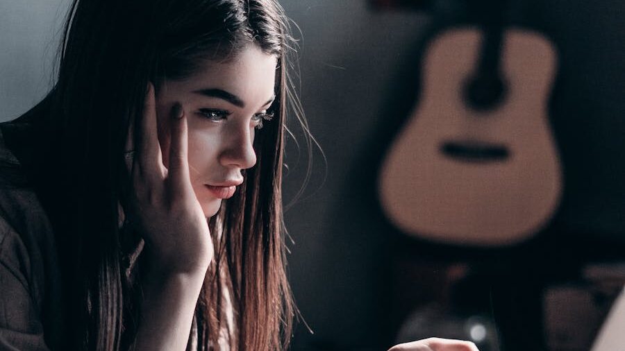 Young woman with long brown hair, resting her face on her hand while looking intently at a screen.