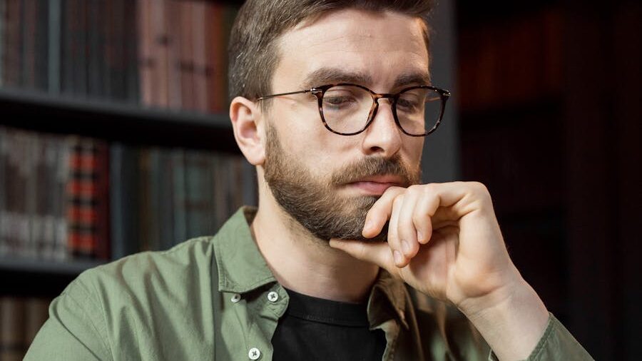 Man with glasses and a beard, wearing a green shirt, resting his chin on his hand in a thoughtful pose.