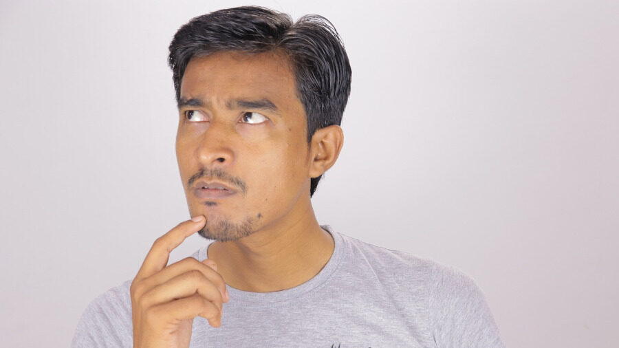A man in a grey t-shirt looking up thoughtfully with a finger on his chin, suggesting deep thinking or curiosity.