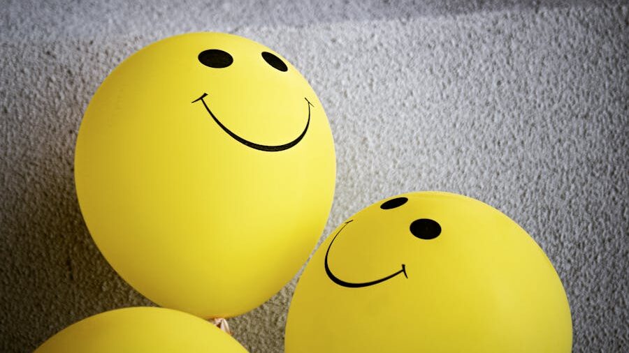 Two yellow balloons with smiley faces close together, leaning toward each other against a gray textured background.