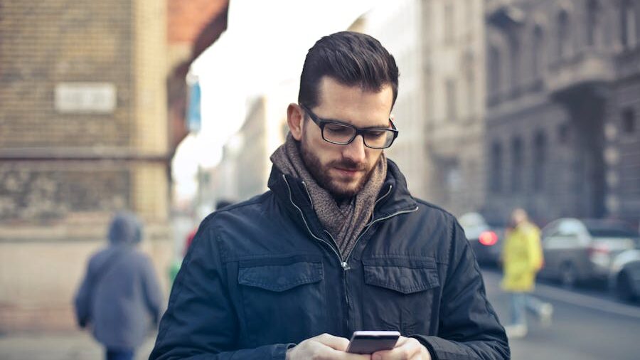 Urban scene with a man using his phone while walking, dressed warmly in scarf and coat on a busy street.