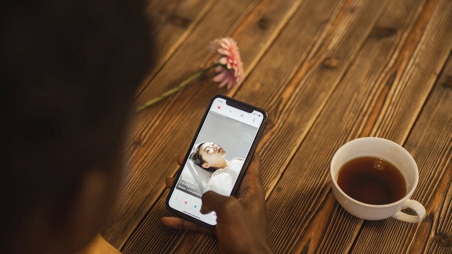 Person holding a smartphone showing an online dating profile, with a cup of tea and a flower on a wooden table.