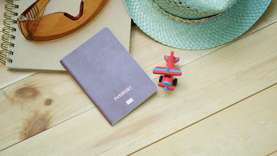 Passport placed on a wooden table beside a toy airplane, hat, sunglasses, and notebook arranged for travel.