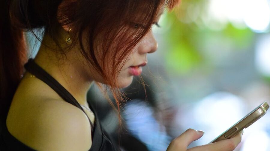 Side-profile close-up of a woman holding a smartphone and looking at the screen, with a blurred background.