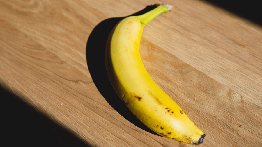 Une banane jaune avec quelques taches brunes, posée sur une surface en bois sous une lumière naturelle.