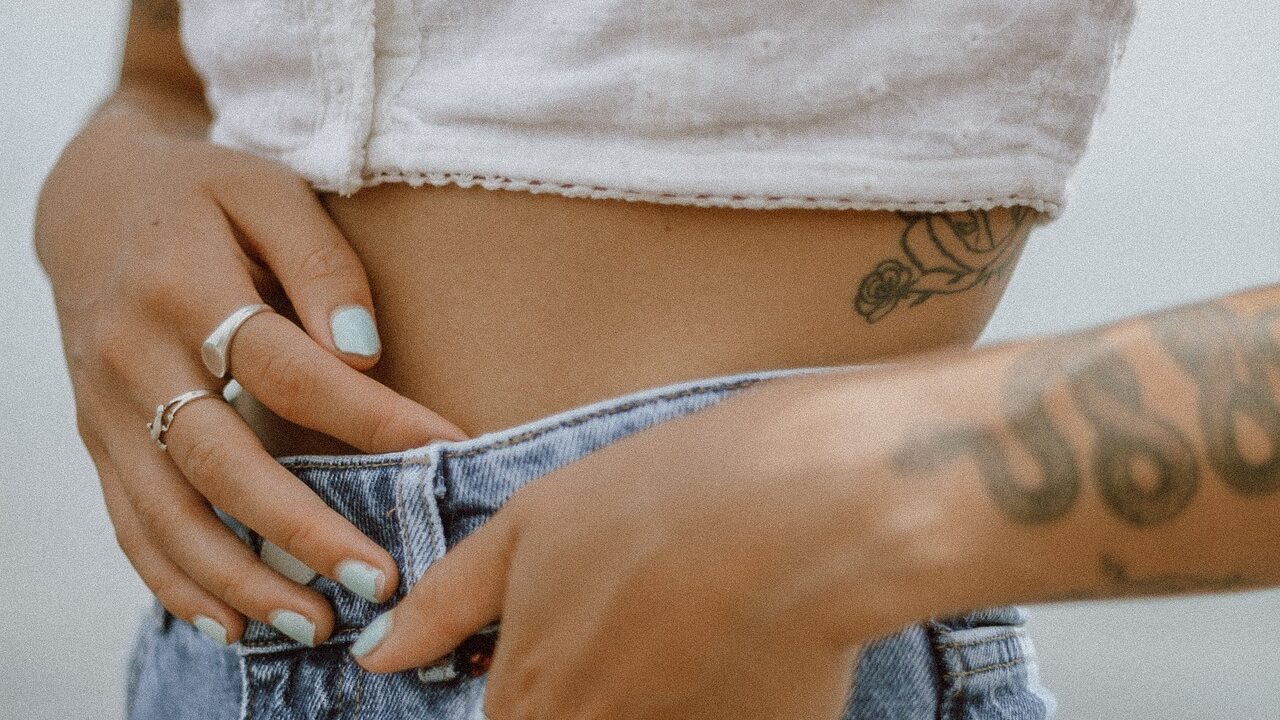 Vue recadrée d'une taille ornée d'un petit tatouage floral, d'un vernis à ongles bleu pâle et d'un jean décontracté.